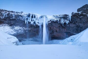 Seljalandsfoss Waterfall appears frozen in winter with ice surrounding the falling water.