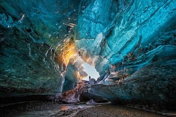 A natural ice cave in Iceland glows with soft light during sunset.