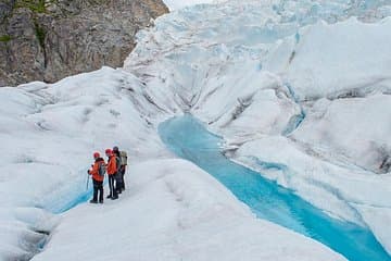 A small team of explorers hikes on a glacier, marveling at the icy crevasses and deep blue ice.