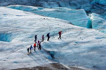 Adventurers walk in a line across a glacier, carefully stepping on the icy surface during a guided glacier hike in Iceland.