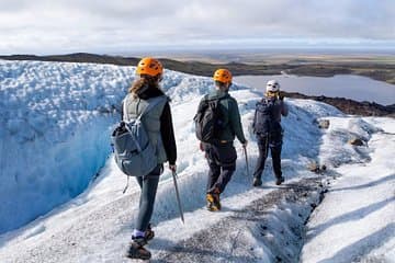 A group of explorers wearing crampons and helmets hikes across a glacier with a view of Skaftafell in the distance.