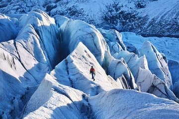 A person stands on a glacier with a rough, cracked ice surface stretching around them.
