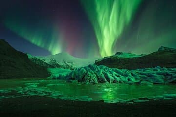 Green northern lights glow above Skaftafell Nature Reserve at night.