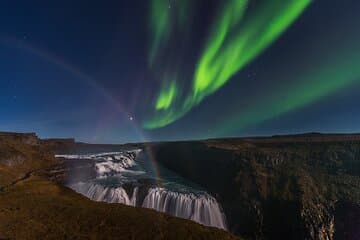 Gullfoss Waterfall flows beneath bright northern lights in the night sky.