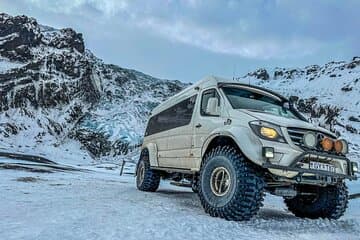 A Super Jeep is parked in a snowy area in Iceland near an ice cave.