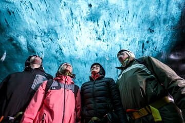 A group of visitors look up in wonder at the ceiling of an ice cave.